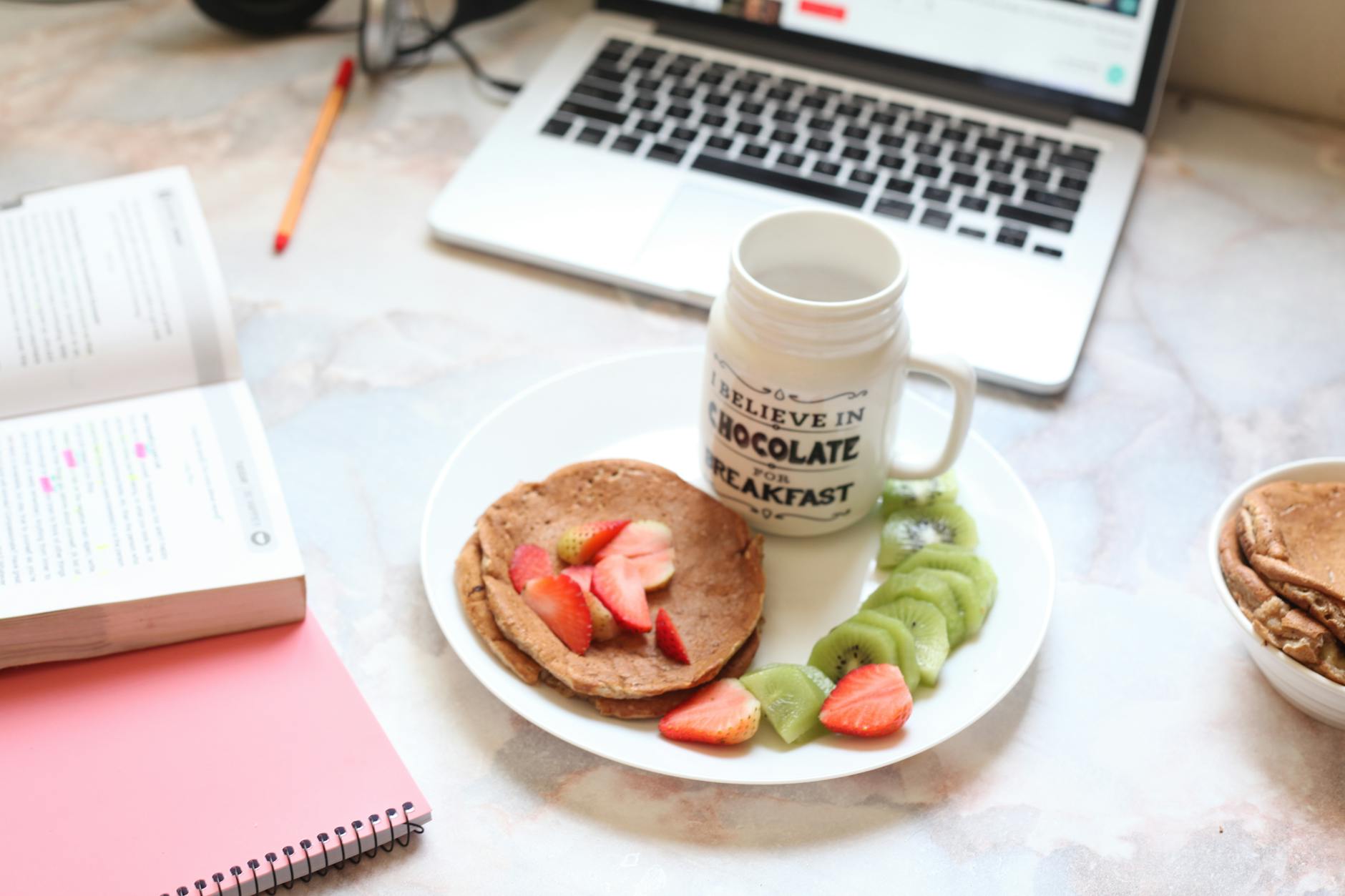 Naleśniki z owocami obok laptopa na biurku w firmowej kuchni
